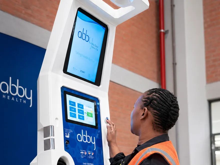 A worker in a hi-vis vest using an Abby health station